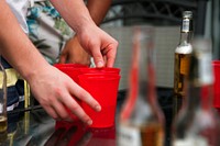 Someone sets up red plactic cups on a table with beer in the background.