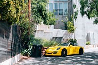 Yellow Porsche sports car parked behind a modern city building covered in plants.