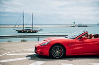 Scarlet red Ferrari with a top down. Older boat in the background.