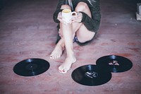 A woman holding a cup of coffee alongside vinyl records on floor