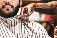 Hairdresser trimming beard of the customer at a barbershop, small business