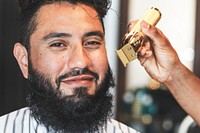 Hairdresser trimming beard of the customer at a barbershop, small business