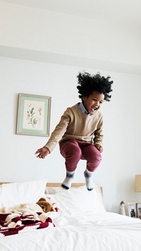 Young happy kid having fun jumping up and down on a bed mobile phone wallpaper