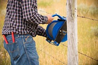 Casey Coulter, landowner in Garfield County, hangs an electric fence wire dispenser on a standing fence on the Coulter Family Ranch in Garfield County. June 2017. Original public domain image from Flickr