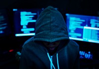 Hacker wearing a hoody with computers in the background 