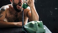 Caucasian topless man yelling over green vintage telephone