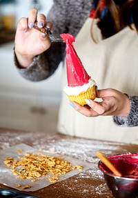 Woman putting icing on a Santa hat cupcake