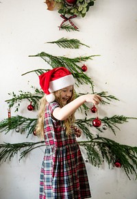 Girl wearing a santa hat hanging up Christmas ornaments