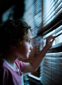 Young boy looking through the window blinds