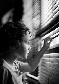 Young boy looking through the window blinds