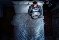 Man on bed using his laptop and a headphone