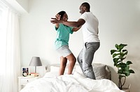 Black couple jumping on bed together