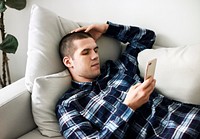 Distressed man laid on the couch using a smartphone