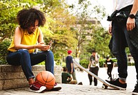 Young adult friends chilling at the park using smartphones and skateboarding youth culture concept