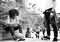 Young adult friends chilling at the park using smartphones and skateboarding youth culture concept