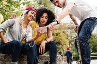 Young adult friends using a smartphone and listening to music outdoors