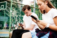 Expressionless young couple in the park using smartphones with no social interactions addiction concept