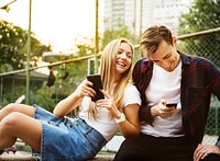 Happy cute young couple in the park using smartphones together