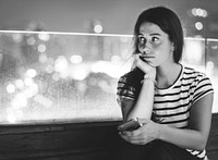 Unhappy young woman holding a smartphone in the evening cityscape