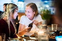Girl friends having a dinner together at a rooftop bar using a smartphone