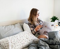 Caucasian woman reading newspaper on bed
