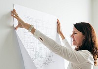 A woman sticking a blueprint to the wall
