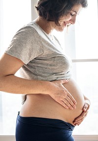 Cheerful pregnant woman standing by the window