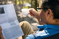 Man relaxing while reading a newspaper and drinking coffee