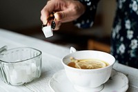 Woman helping herself with a sugar cube for her cup of nice hot lemon tea