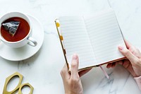 Aerial view of hot tea drink and woman holding blank journal copy space