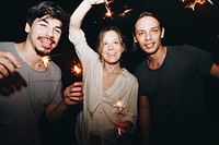 Two Caucasian men and a woman playing with sparklers celebration and festive party concept