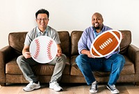 Men holding baseball and rugby icons sitting on couch