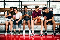 Group of young teenager friends on a basketball court relaxing using smartphone