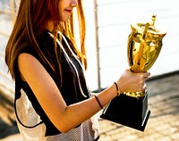 Asian teenage girl in sporty clothes holding a trophy outdoors