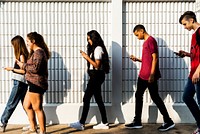Group of diverse teenagers using phones while walking