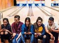 Group of teenage friends using smartphone in a bowling alley