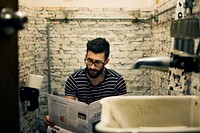 Man in a restroom reading newspaper