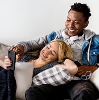 Cute interracial couple on a couch sharing smartphone love, internet and music concept