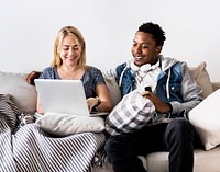 Cute interracial couple on a couch sharing laptop love, internet and music concept