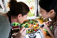 Two women cooking healthy vegetables in a pan