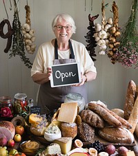 Elderly woman showing open sign at a deli
