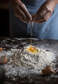 Baker breaking an egg into a flour mixture