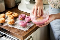 Woman hand coating fried donuts with pink frosting