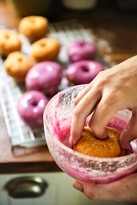 Woman hand coating fried donuts with pink frosting