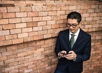 Businessman using a smartphone next to a brick wall
