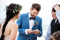 Groom occupied with phone at beach wedding ceremony