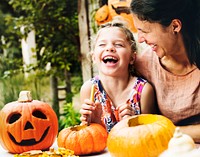 Young cheerful girl carving pumpkins with her mom