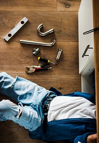 Plumber lying on the floor fixing a kitchen sink