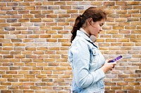 Teen girl texting on her phone by a brick wall