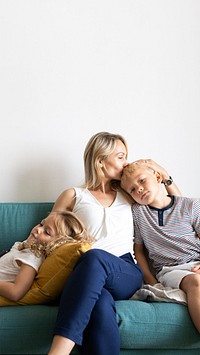 Blonde mom kissing her son&rsquo;s head and relaxing with daughter on the couch blank space 